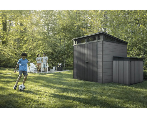 Záhradná scéna s kôlňou na náradie a rodinou na trávniku