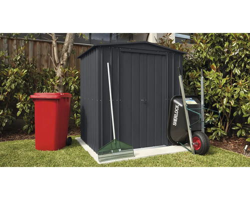 Záhradná scéna s domčekom na náradie, smetným košom, fúrikom a hrabľami vonku.