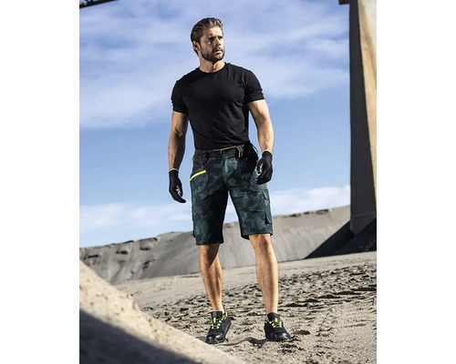 Muž má na sebe čierne tričko, pracovné rukavice, krátke pracovné nohavice s maskovacím vzorom a pracovné topánky.