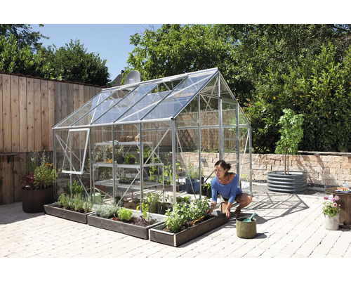 Skleník s rastlinami a ženou pracujúcou v záhrade.