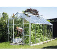 Skleník v záhrade so ženou zalievajúcou rastliny