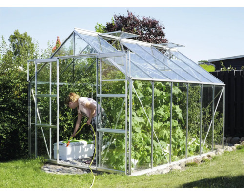 Skleník v záhrade so ženou zalievajúcou rastliny