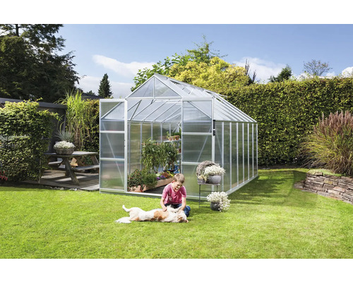 Skleník v záhrade s hrajúcim sa dieťaťom a psom na trávniku.