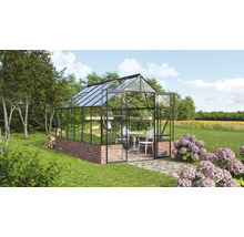 Skleník s tehlovým základom, sklenenými stenami a stolom so stoličkami vnútri záhrady.