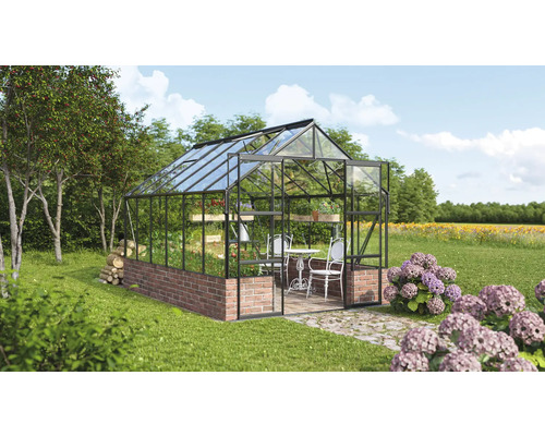 Skleník s tehlovým základom, sklenenými stenami a stolom so stoličkami vnútri záhrady.