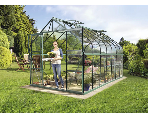 Skleník v záhrade so ženou nesúcou rastlinu.