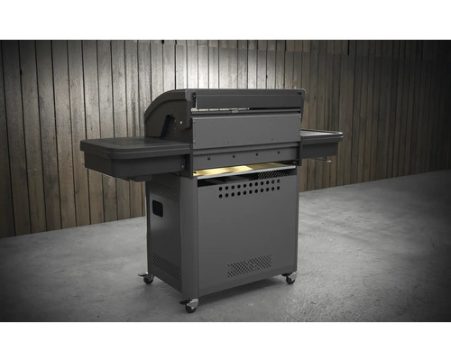 Tmavosivý gril na kolieskach s bočnými policami a kolieskami pred drevenou stenou