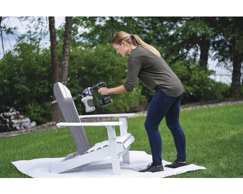 Žena natiera drevenú stoličku striekacou pištoľou na farbu v záhrade