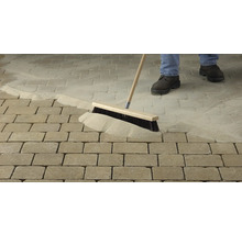 Osoba zametá dlažobný piesok do škár dlaždenej cesty metlou