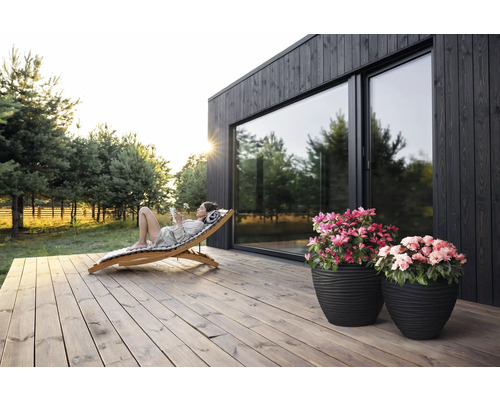 "Scéna so ženou odpočívajúcou na drevenom ležadle na drevenej terase pred domom s veľkými oknami