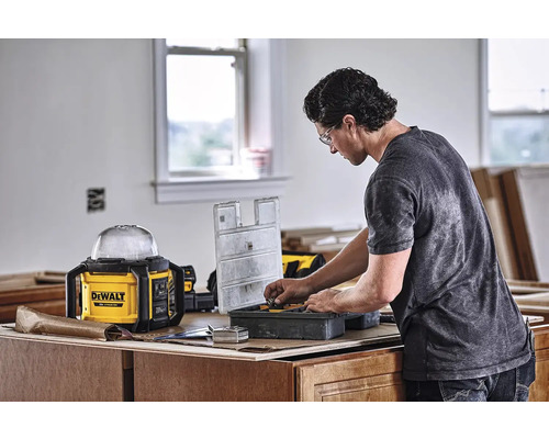 Remeselník triedi nástroje v debne na náradie. V pozadí je pracovná lampa značky Dewalt.