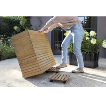 Osoba pohybuje dreveným kvetináčom na kolieskovej doske v záhrade.