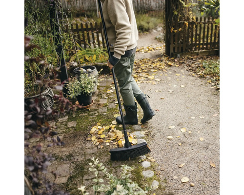 Osoba zametá lístie pouličnou metlou v záhrade.