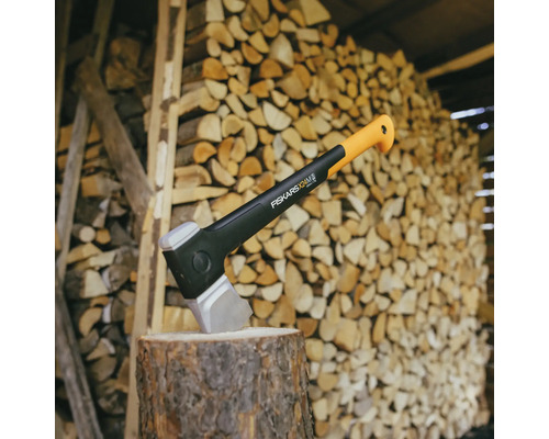 Štiepacia sekera Fiskars na kláte pred hromadou dreva