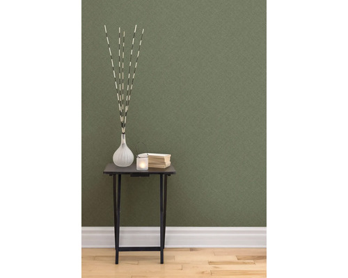 Dekoratívna scéna so stolom, vázou, sviečkou a knihami na pozadí štruktúrovanej tapety