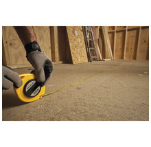 Osoba meria drevenú miestnosť pomocou 30-metrového zvinovacieho metra Stanley.