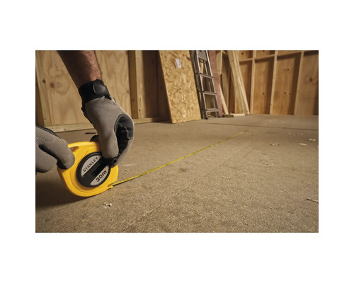 Osoba meria drevenú miestnosť pomocou 30-metrového zvinovacieho metra Stanley.