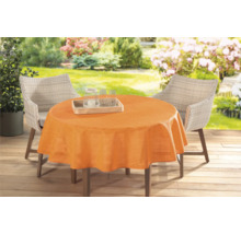 Záhradný stôl s oranžovým obrusom a ratanovými stoličkami vonku.
