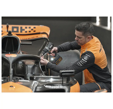 Muž pripevňuje niečo k pretekárskemu autu pomocou akumulátorového skrutkovača.