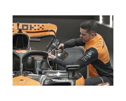 Muž pripevňuje niečo k pretekárskemu autu pomocou akumulátorového skrutkovača.