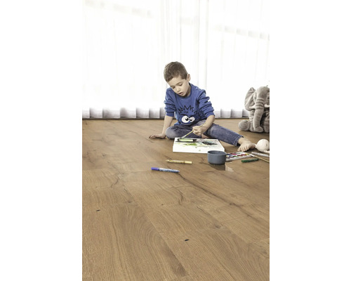 Dieťa maľuje na drevenej podlahe. V pozadí je plyšový slon.