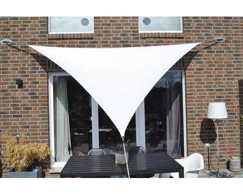 Trojuholníková slnečná plachta nad terasovým stolom so stoličkami pri stene domu