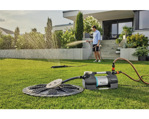 Scéna so záhradným čerpadlom, zavlažovačom a osobou zavlažujúcou záhradu na trávniku