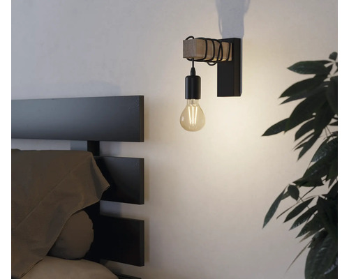 Nástenné svietidlo s drevenými a kovovými prvkami vedľa postele