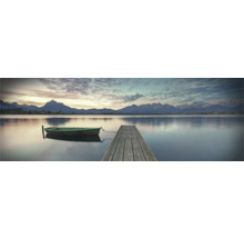 Kojné jazero s dreveným mólom a malou loďou v popredí, s horskou krajinou v pozadí.