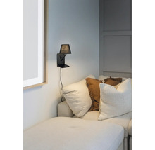 Nástenná lampa s malým tienidlom vedľa pohovky s vankúšmi