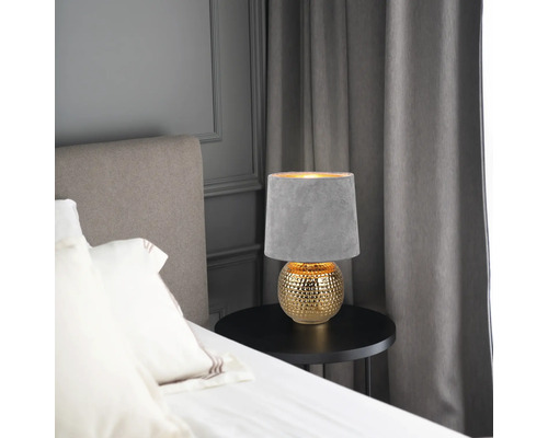 Nočná lampa so sivým tienidlom a zlatou základňou na stole