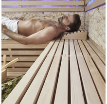 Muž relaxuje v saune s drevenými lavicami a príslušenstvom.