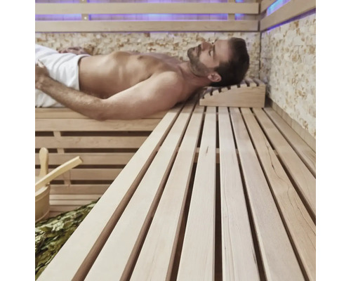 Muž relaxuje v saune s drevenými lavicami a príslušenstvom.