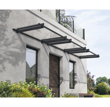 Moderná vchodová strieška s tmavým kovovým rámom a priehľadnými panelmi nad vchodovými dverami a oknami na sivej kamennej fasáde.