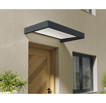 Moderná vchodová strieška v antracitovej farbe s bielou výplňou inštalovaná nad drevenými vchodovými dverami na omietnutej stene.