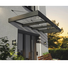 Moderná strieška zo skla a kovu nad terasovými dverami na stene domu s nástennými svietidlami a drevenou lavičkou.