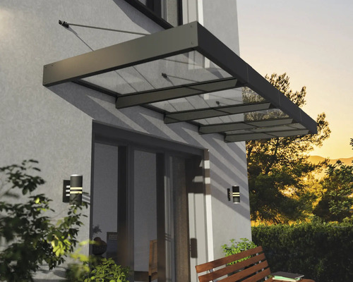 Moderná strieška zo skla a kovu nad terasovými dverami na stene domu s nástennými svietidlami a drevenou lavičkou.