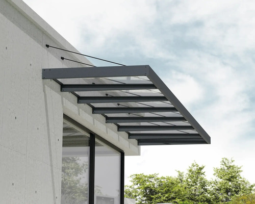 Moderná vchodová strieška zo skla s antracitovým hliníkovým rámom a lankovým zavesením na svetlej fasáde.