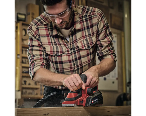 Muž hobľuje drevo elektrickým hoblíkom Einhell v dielni.