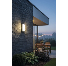 Osvetlená terasa s nástenným svietidlom, dreveným stolom a svetelnou reťazou v záhrade