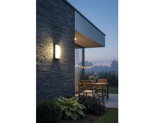 Osvetlená terasa s nástenným svietidlom, dreveným stolom a svetelnou reťazou v záhrade