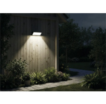 Vonkajší pohľad na dom so svietiacou nástennou lampou, obklopený rastlinami a chodníkom