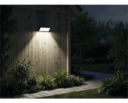 Vonkajší pohľad na dom so svietiacou nástennou lampou, obklopený rastlinami a chodníkom