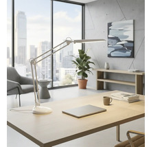 Svetlá kancelária s písacím stolom, stolnou lampou, notebookom, rastlinou a oknom s výhľadom na mesto