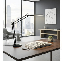 Stôl s lampou s otočným ramenom, knihou a perami vo svetlej kancelárii.