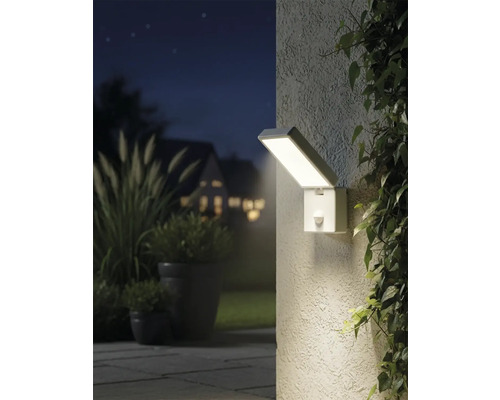 Osvetlený vonkajší záber s obdĺžnikovým nástenným svietidlom so senzorom pohybu vedľa rastlín.