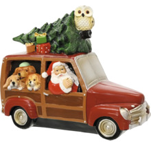 Vianočná figúrka Santa Claus za volantom červeného auta s tromi psami, vianočným stromčekom, darčekmi a sovou na streche.