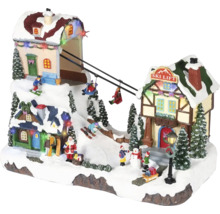 LED osvetlená vianočná dedinka s pohyblivým lyžiarskym vlekom, zasneženými domami, jedličkami a figúrkami ako Santa Claus a lyžiari.