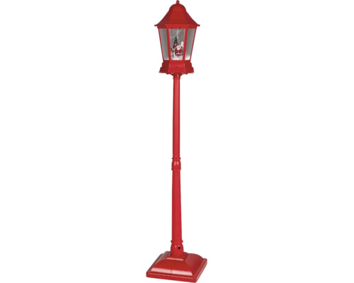 Červená vianočná pouličná lampa s efektom snehovej gule, figúrkou Santa Clausa a vianočným stromčekom.