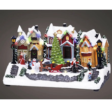 Zasnežená vianočná krajina s osvetlenými miniatúrnymi domami, vianočným stromčekom, saňami, sobom a figúrkami.